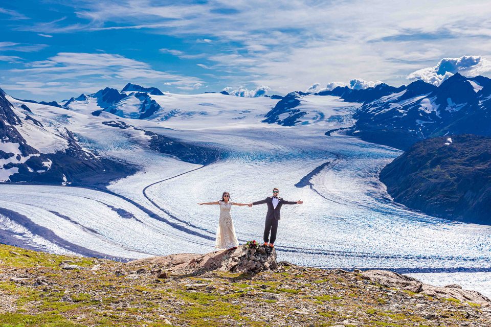 A couple holding hands in front of an Alaska glacier.